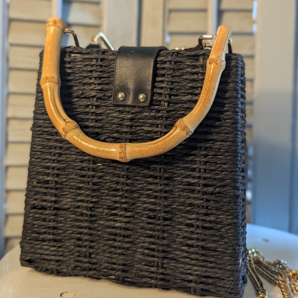 Black woven handbag with bamboo handle and gold chain strap
